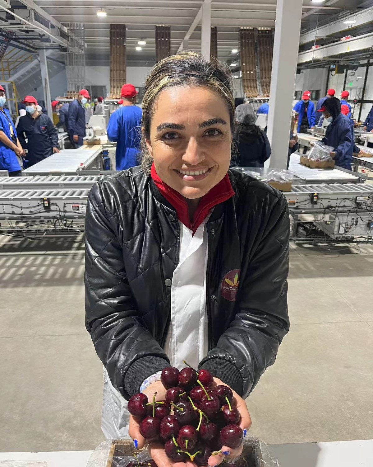 Fiorella Bonino con chaqueta Dancing Sun sosteniendo cerezas frescas en línea de packing junto al equipo operativo